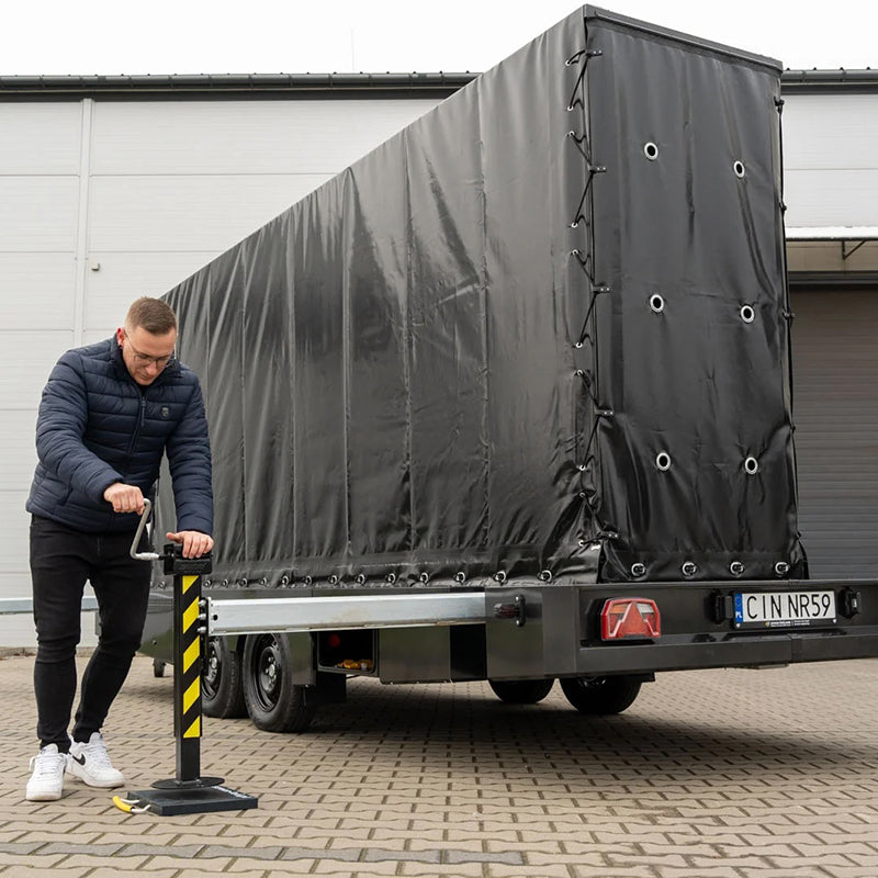Schwarzer LED Trailer Veranstaltungstechnik mit Plane und Mann, der Stützfuß an Hebel bedient vor Industriegebäude