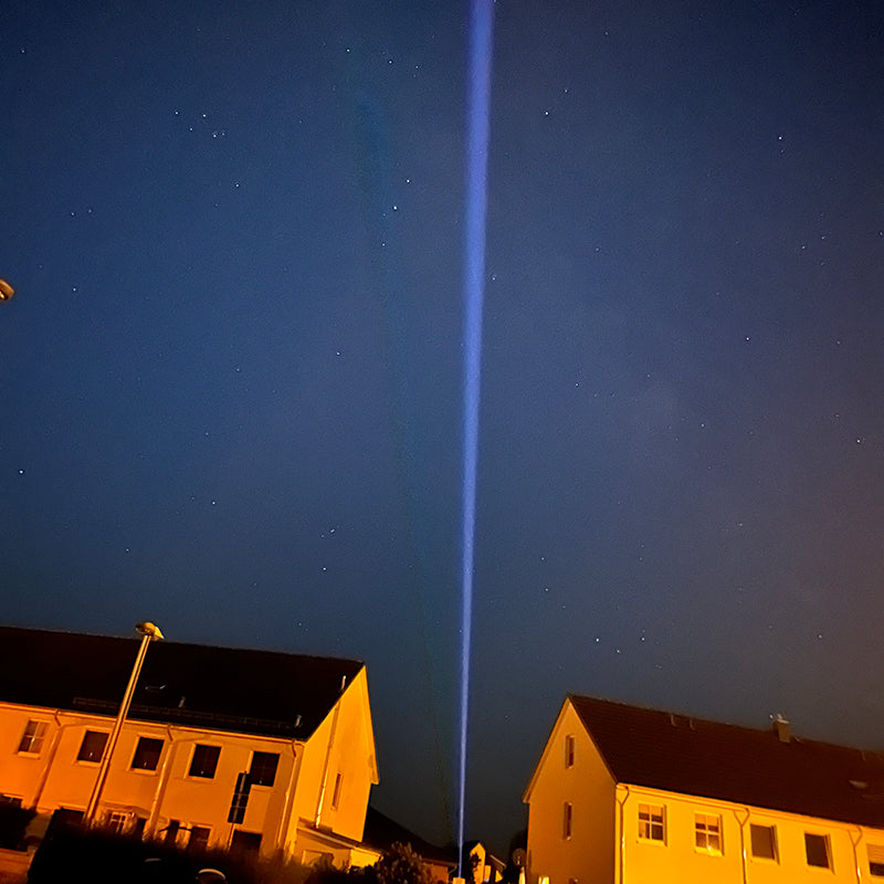 Starke blaue Lichtstrahlen nachts über Wohnhäusern als Lichttechnik für Outdoor Veranstaltungen