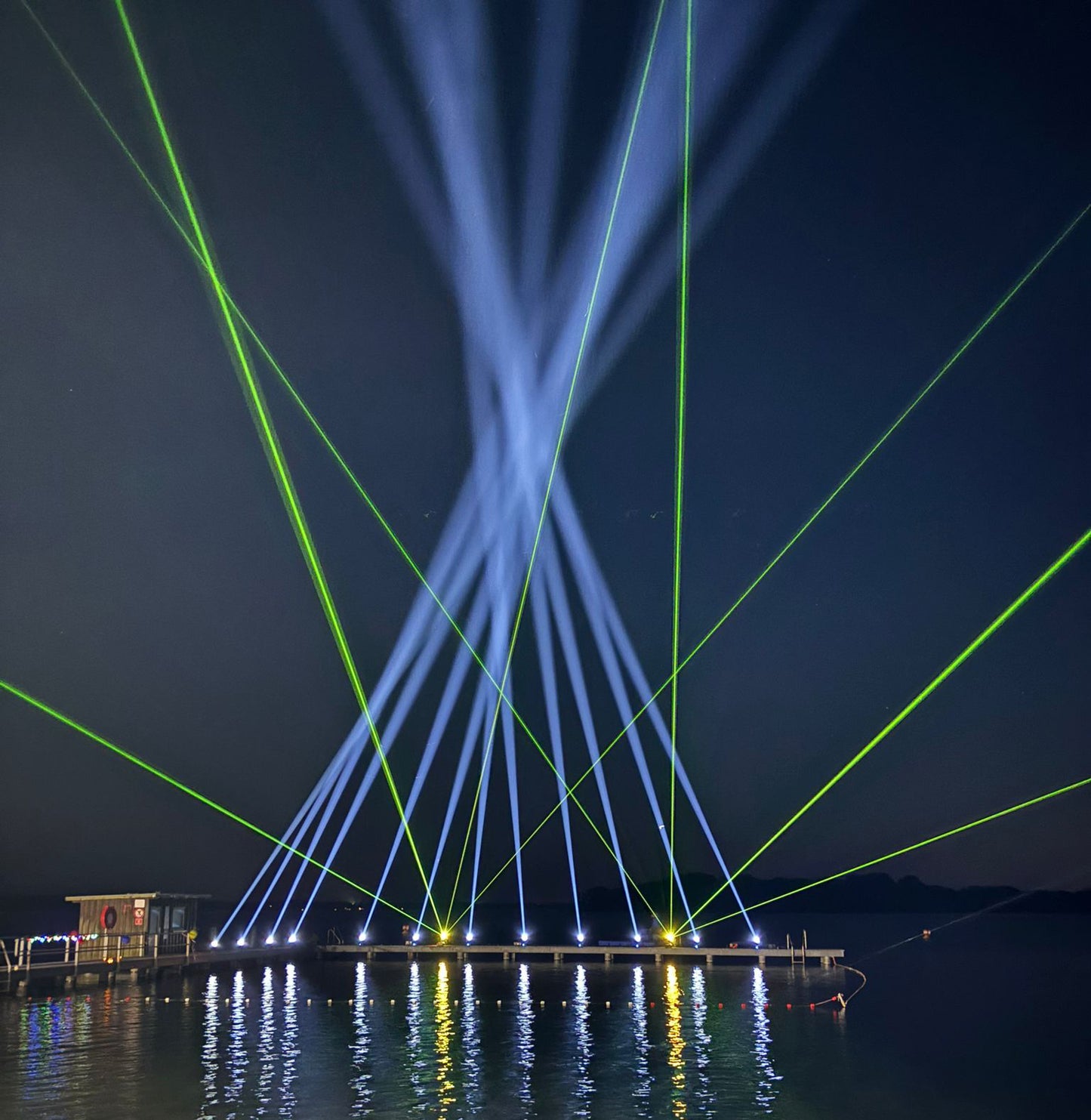 Lichttechnik für Outdoor Veranstaltungen mit blauen und grünen Lichtstrahlen über Wasser in der Nacht